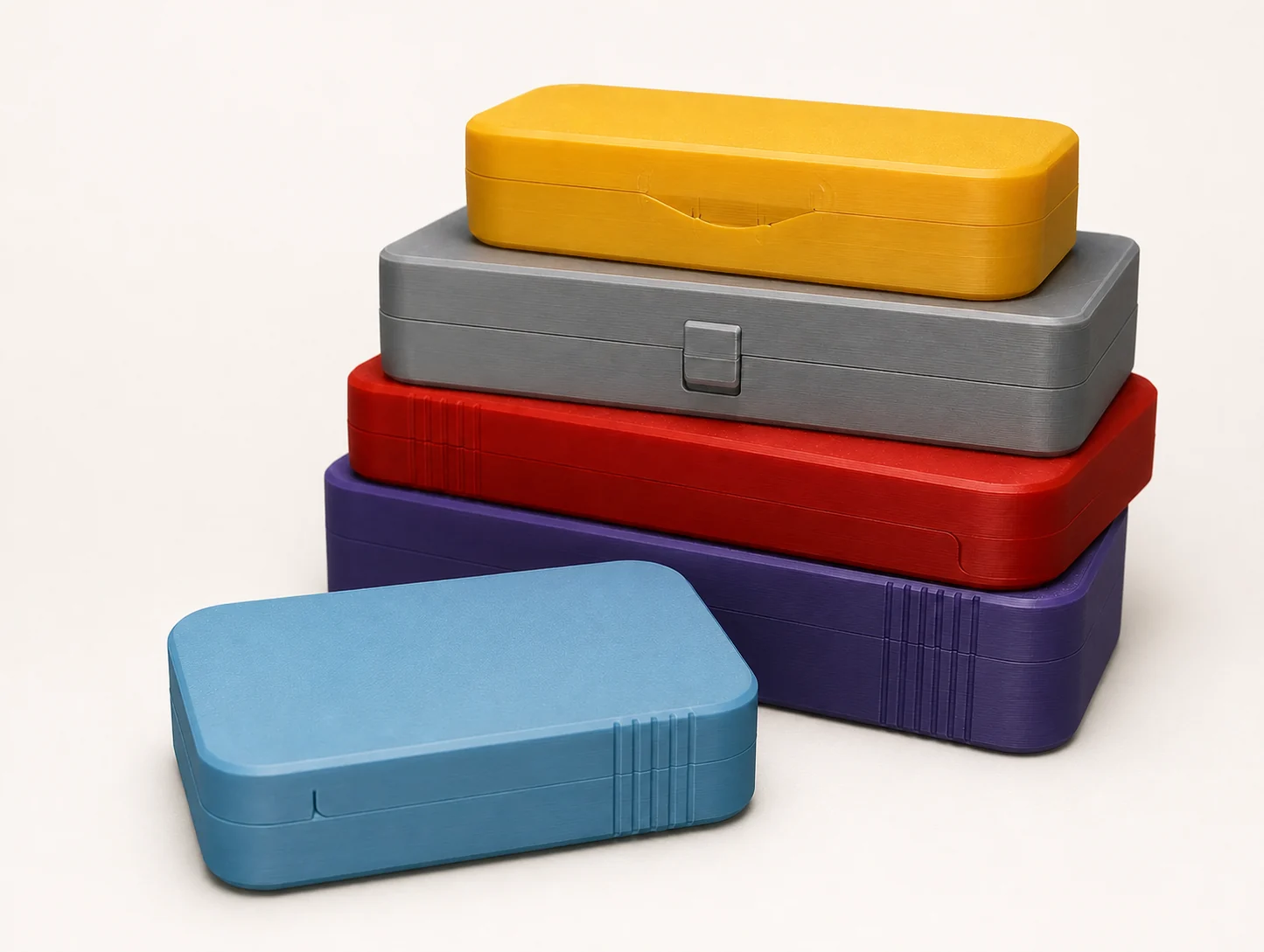 Pile de boîtes imprimées en 3D de différentes tailles et couleurs : jaune, grise, rouge, violette et bleue