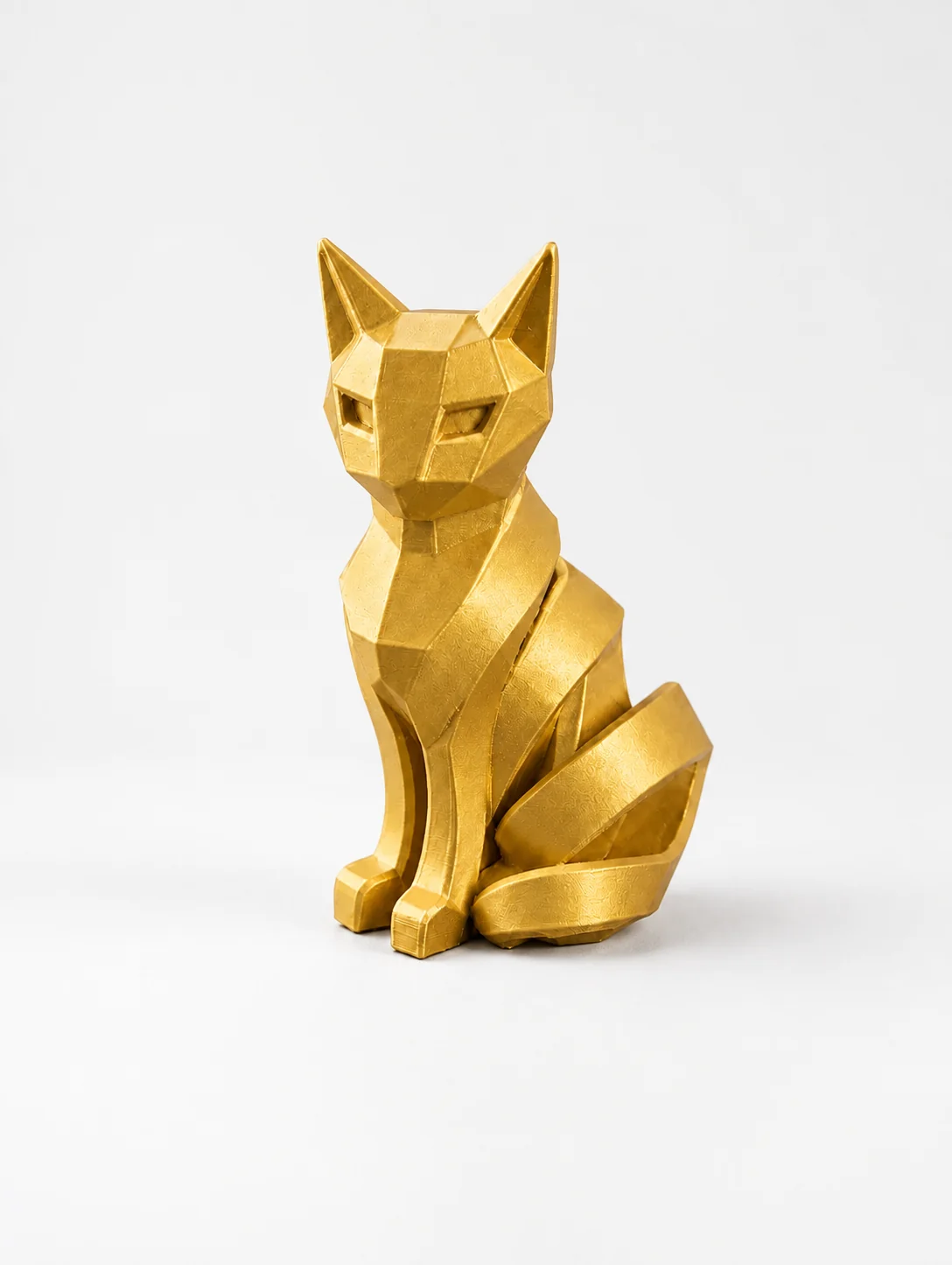 Chat low-poly doré imprimé en 3D, facettes géométriques, assis