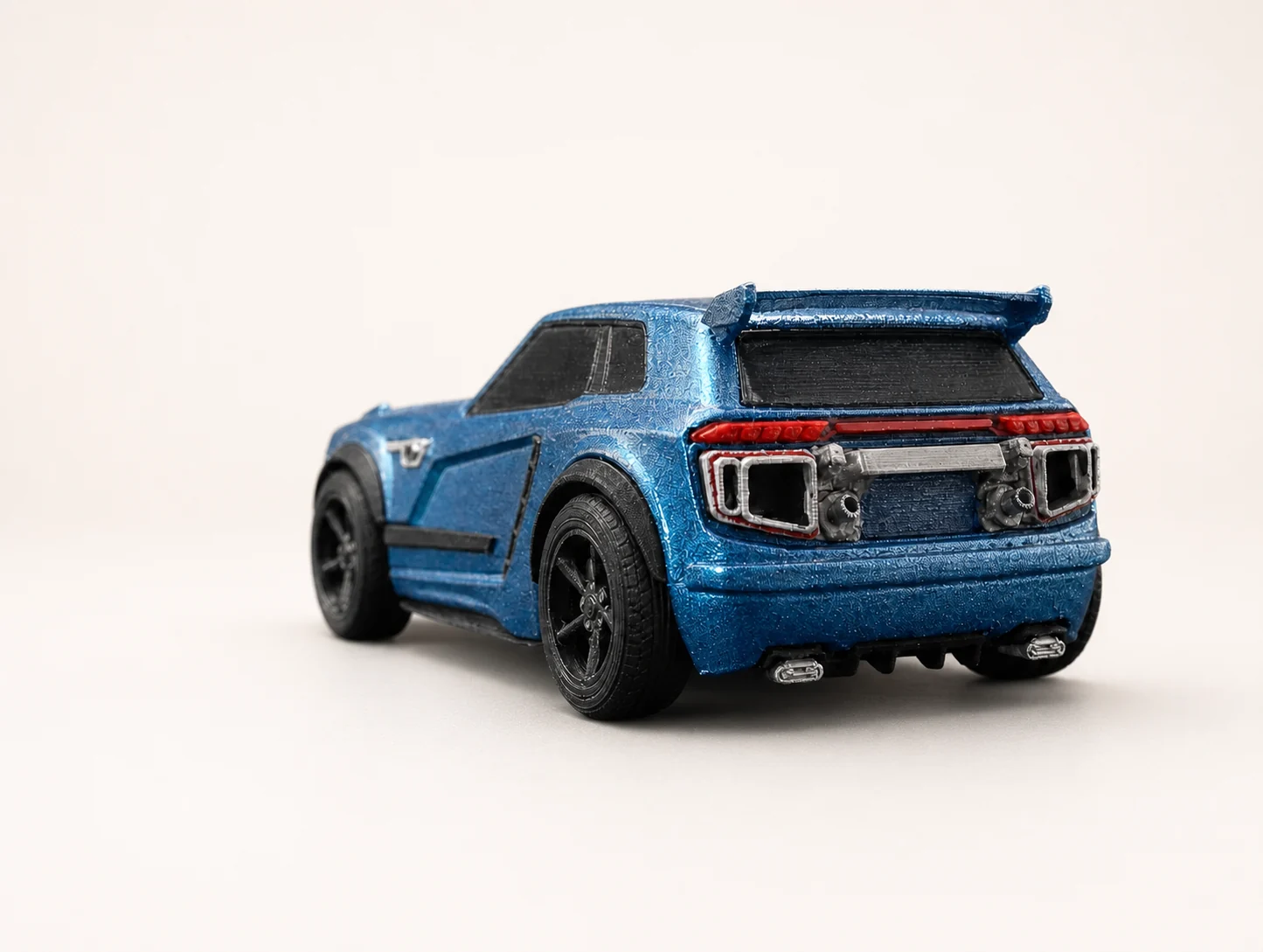 Voiture miniature bleue imprimée en 3D vue de l'arrière, aileron et feux détaillés