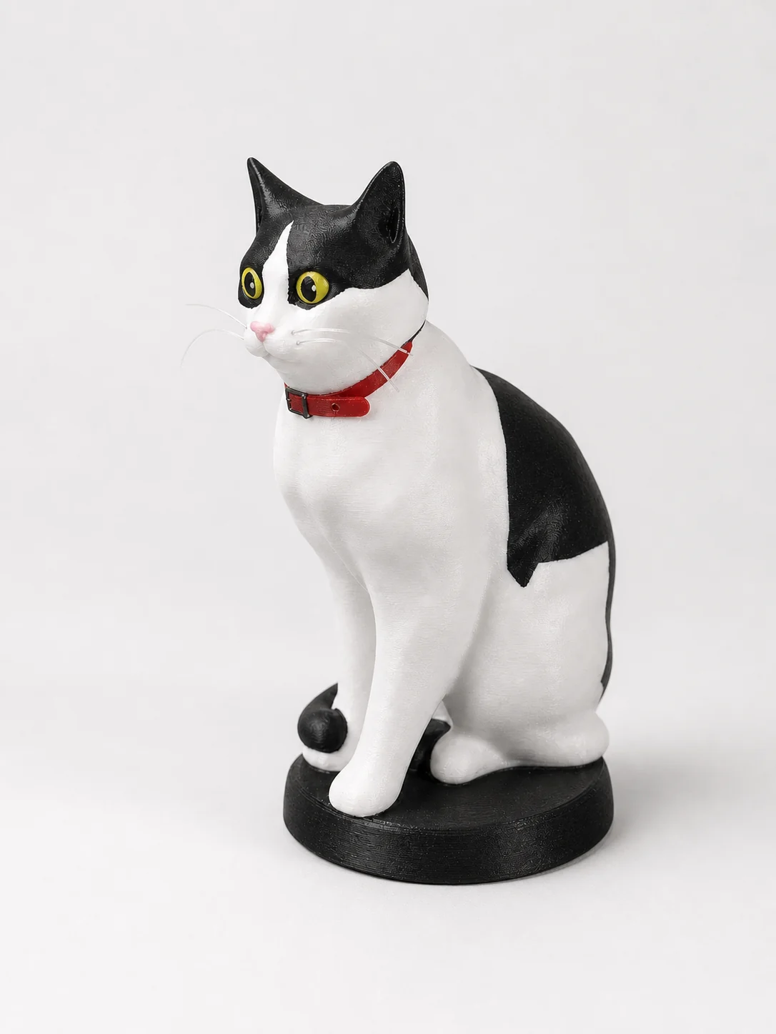 Figurine de chat noir et blanc au collier rouge, imprimée en 3D, assise sur un socle noir